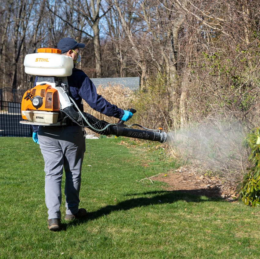 view from the back as a ProSource Pest tech sprays a yard with insecticides in Southington, CT